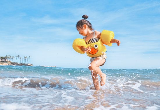An image of a little girl playing in the ocean on holiday, wearing yellow armbands