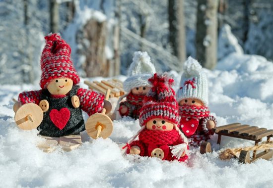 An image of little cute wooden dolls wearing wool hats and sat in the snow