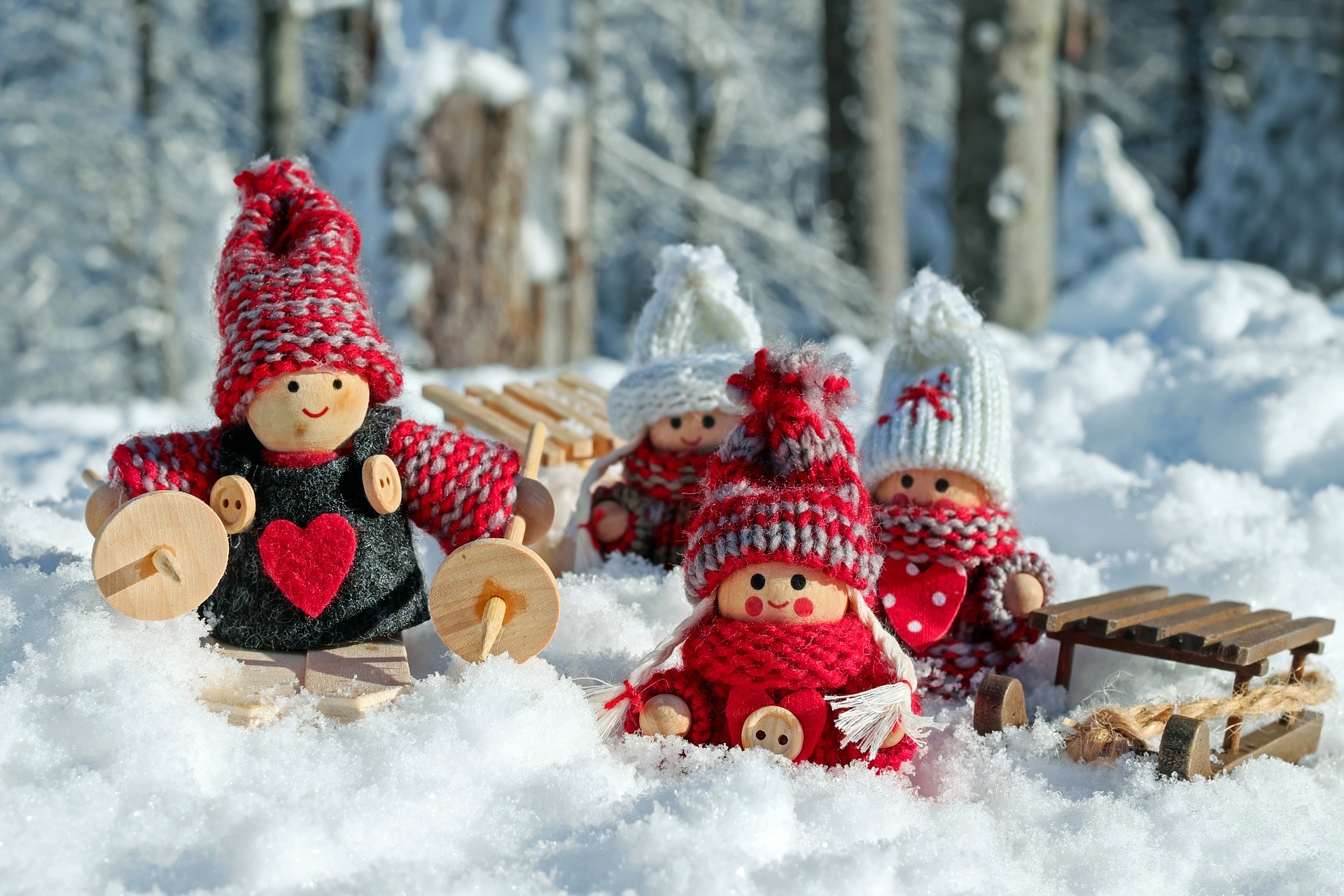 An image of little cute wooden dolls wearing wool hats and sat in the snow